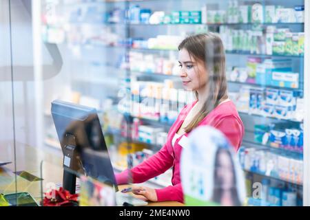 Young pharmacist working on desktop PC at checkout counter Stock Photo