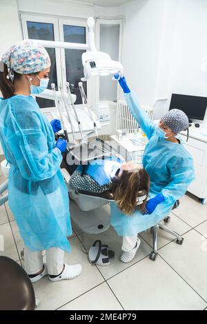 Young dentist and assistant examining patient through equipment at clinic Stock Photo