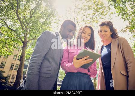 Smiling businesswomen and businessman using tablet PC in park Stock Photo