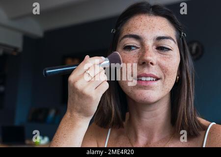 Woman with freckle face applying makeup at home Stock Photo