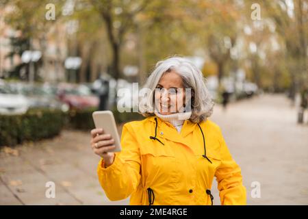 Happy senior woman using smart phone at footpath Stock Photo