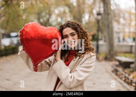 Happy woman with red heart shaped balloon at footpath Stock Photo