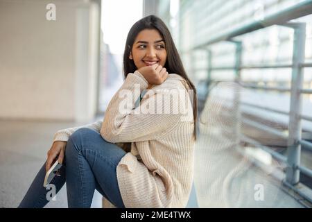 Thoughtful young woman sitting by glass wall Stock Photo