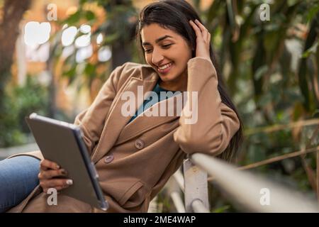 Happy woman using tablet PC sitting by railing Stock Photo