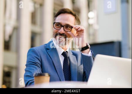 Smiling mature businessman adjusting eyeglasses sitting in cafe Stock Photo