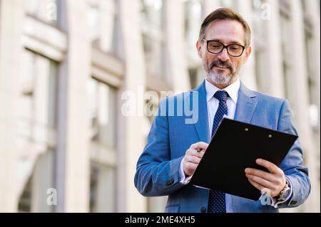Smiling businessman with clipboard standing outside building Stock Photo