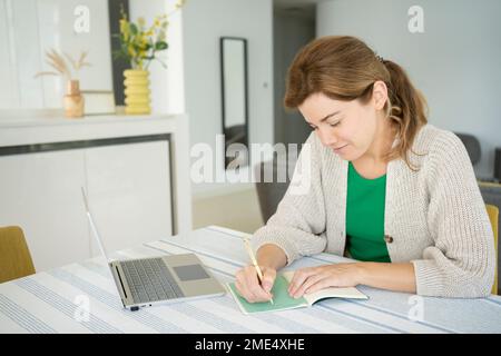 Freelancer woman making notes in note pad on desk at home office Stock Photo