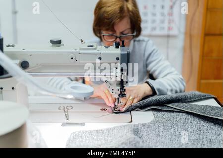 Senior craftswoman using sewing machine in workshop Stock Photo