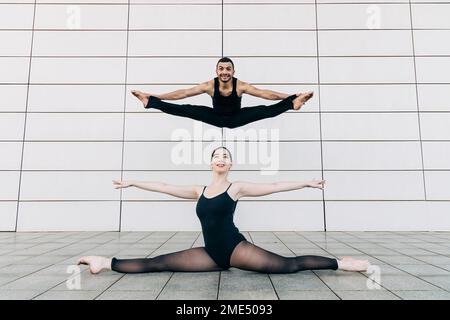 Happy man and young woman doing splits in front of tiled wall Stock Photo
