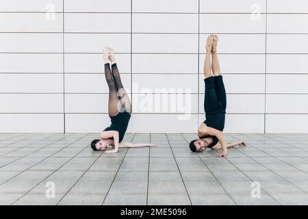 Couple doing headstand together in front of wall Stock Photo