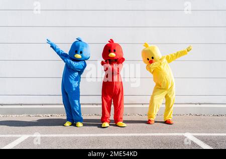 Carefree friends wearing multi colored duck costumes standing in front of wall Stock Photo