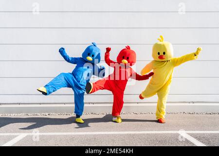 Friends wearing multi colored duck costumes enjoying in front of wall Stock Photo