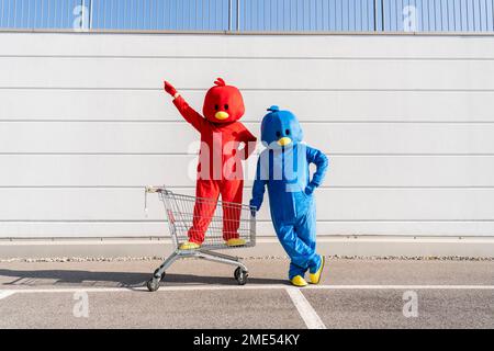 Man and woman wearing duck costumes standing with shopping cart in front of wall Stock Photo