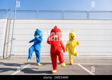 Friends wearing duck costumes dancing in front of wall on sunny day Stock Photo