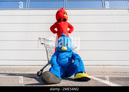 Woman wearing red duck costume standing in front of wall with man sitting on ground Stock Photo