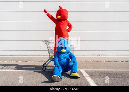 Woman wearing red costume standing in shopping cart with man sitting on ground Stock Photo