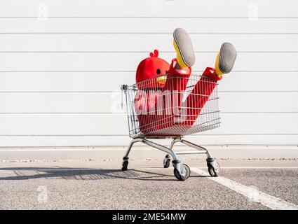 Woman wearing red duck costume sitting in shopping cart in front of wall Stock Photo