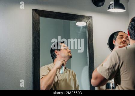 Man with electric razor shaving in bathroom Stock Photo
