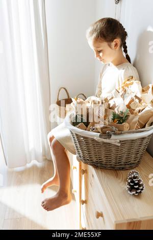 Girl opening gifts sitting on cabinet by basket of advent calendar at home Stock Photo