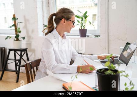Smiling mature engineer using laptop and working at desk in office Stock Photo