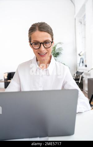 Happy businesswoman wearing eyeglasses using laptop in office Stock Photo