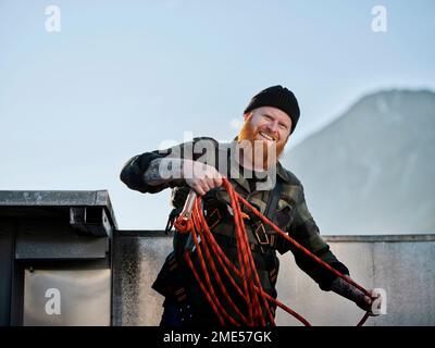 Happy roofer working with rope at rooftop Stock Photo