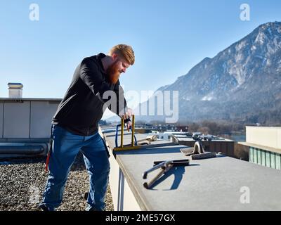 Young roofer with work tools working on roof Stock Photo