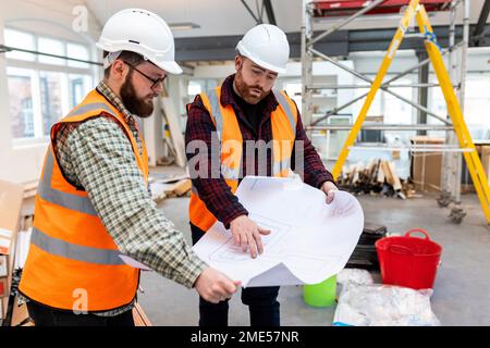 Young engineers wearing hardhats discussing over blueprint at construction site Stock Photo