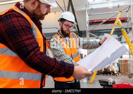Engineer discussing over blueprint with colleague at construction site Stock Photo
