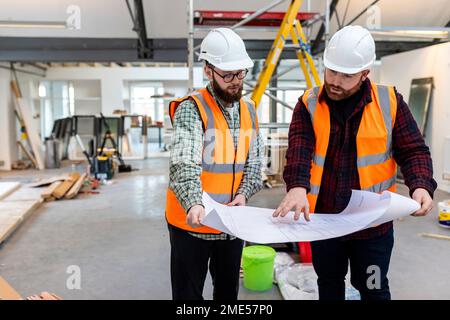 Engineer having discussion over blueprint with colleague at construction site Stock Photo