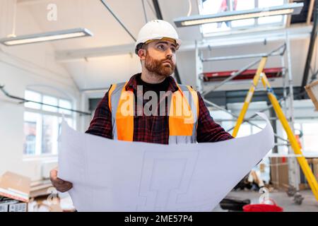 Young engineer standing with blueprint at construction site Stock Photo