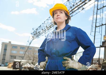 Waist up portrait of empowered woman working at construction site standing against sky with tower crane in background, copy space Stock Photo