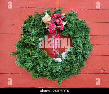 Green Christmas wreath with a plaid bow and melting snow on a red barn Stock Photo