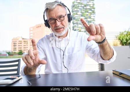 Older senior business man wearing headphones having hybrid work call. Stock Photo