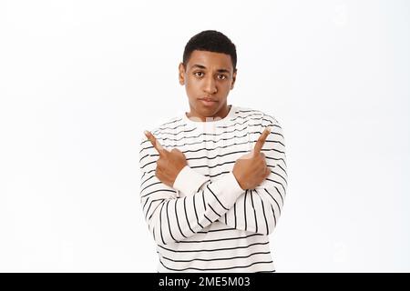 Complicated Black man pointing sideways, showing left and right way, choosing between two products, standing over white background Stock Photo