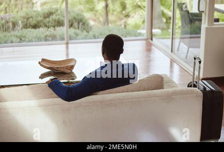 Thinking, immigration and vision of businessman on a couch or sofa in a hotel sitting looking at a window. Rear view, travel and back of professional Stock Photo