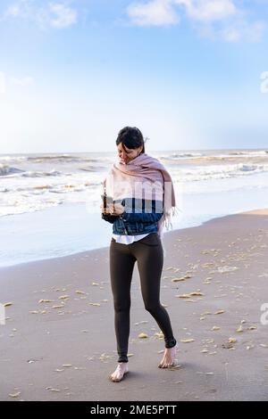 Shot of a  woman using a mobile phone while walking on the beach Stock Photo