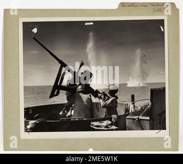 Coast Guardsmen in Action at New Britain. U.S. Coast Guardsmen fight off attacking Japanese planes during the invasion of Cape Gloucester, New Britain. Behind the gun a Coast Guardsman can be seen pointing at a plane overhead. How nearly successful the Japanese were in their attempt to hit the Coast Guard manned LSTs (Landing ship, tanks) can be seen from the bomb splashes. Stock Photo