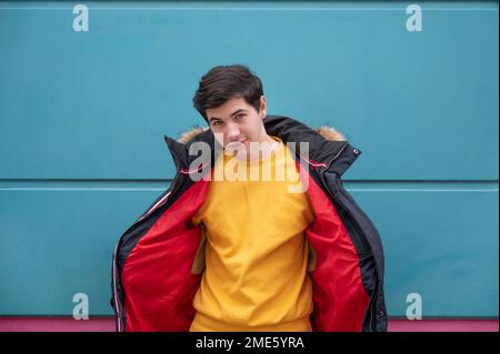 A young man in a yellow sweater and a red jacket on a blue background. Stock Photo