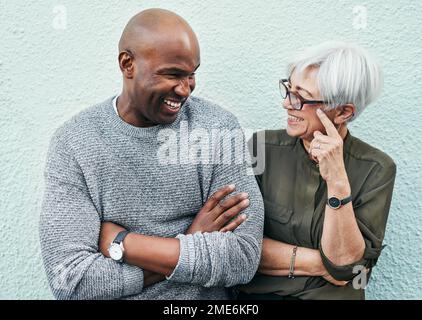 We just have our own little understanding. two cheerful mature businesspeople having a discussion while standing against a wall outdoors. Stock Photo