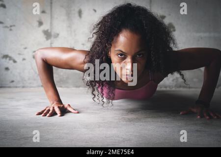 Shes pushing herself to the limit. Portrait of an attractive young sportswoman doing push ups while exercising inside a parking lot. Stock Photo