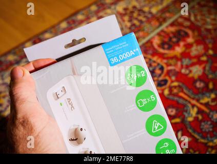 Frankfurt, Germany - Dec 2, 2022: POV male customer hand holding APC American Power Conversion Corporation by Schneider Electric cardboard package of new surge protector featuring 2 USB, 5 outlets and 1.8 meter cable up to 26000 Amperes Stock Photo