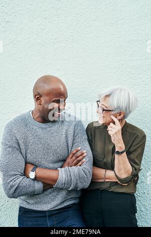 Inside jokes are always the funniest. two cheerful mature businesspeople having a discussion while standing against a wall outdoors. Stock Photo