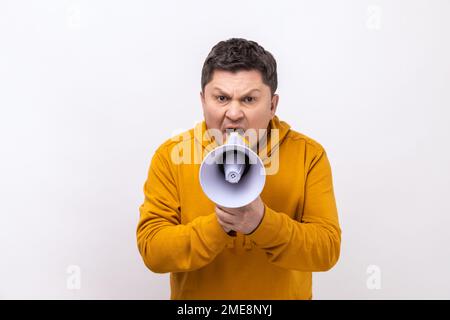 Portrait of dark haired middle aged handsome man screaming in megaphone, announcing important information, wearing urban style hoodie. Indoor studio shot isolated on white background. Stock Photo