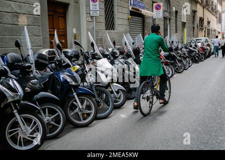 Man riding bicycle while on mobile phone, passing sidewalk lined with scooters in Florence, Italy. Stock Photo