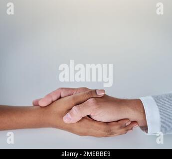 It costs nothing to lend a helping hand. a businessman and businesswoman compassionately holding hands at a table. Stock Photo