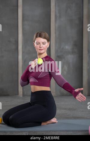 A young woman in sportswear does self-massage and presses on trigger points with a ball after training. MFR Stock Photo