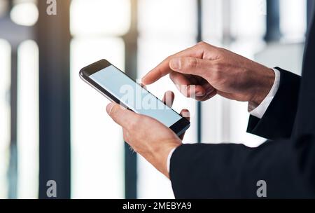 The business device that does it all. an unrecognisable businessmen using a smartphone in a modern office. Stock Photo