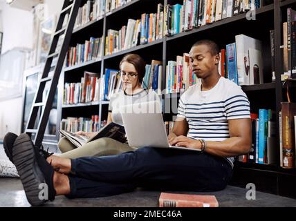Knowledge is everywhere if you seek it. two young sitting on the floor and studying in a college library. Stock Photo