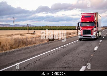 Industrial long hauler big rig red semi truck tractor with truck driver sleeping compartment transporting cargo in dry van semi trailer driving on the Stock Photo